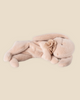 A Maileg Plush Sleeping Bunny - Powder, crafted from soft cotton fabric, lies on its side with long ears and eyes gently closed. It features a small flower decoration near its neck, set against a plain beige background. This charming piece ships in one week.