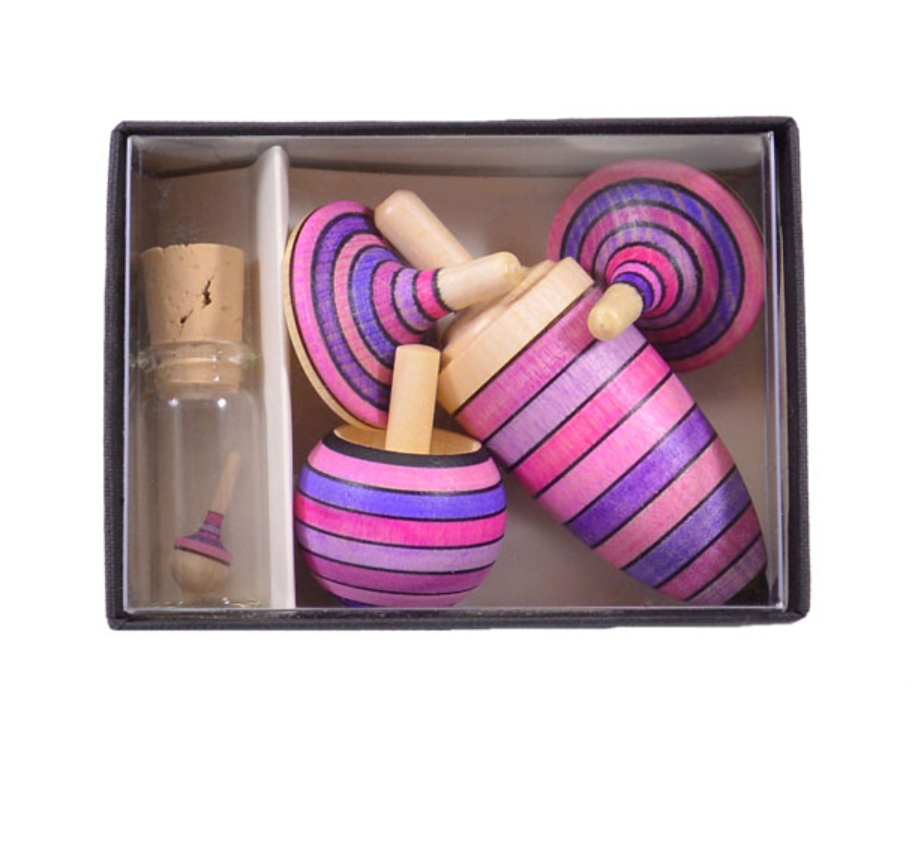 The Mader Spinning Top Champion Learning Set - Lilac includes three striped spinning tops in pink, purple, and black, a matching miniature top, and a corked glass vial—all crafted to meet toy safety standards.