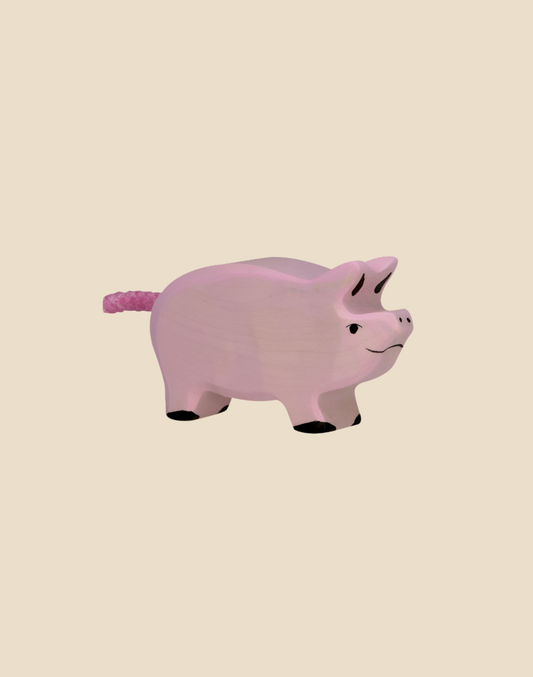 The Holztiger Piglet is a handcrafted wooden toy painted light pink with watercolors, featuring black hooves, a smiling face, and a textured pink tail. Ships in one week.