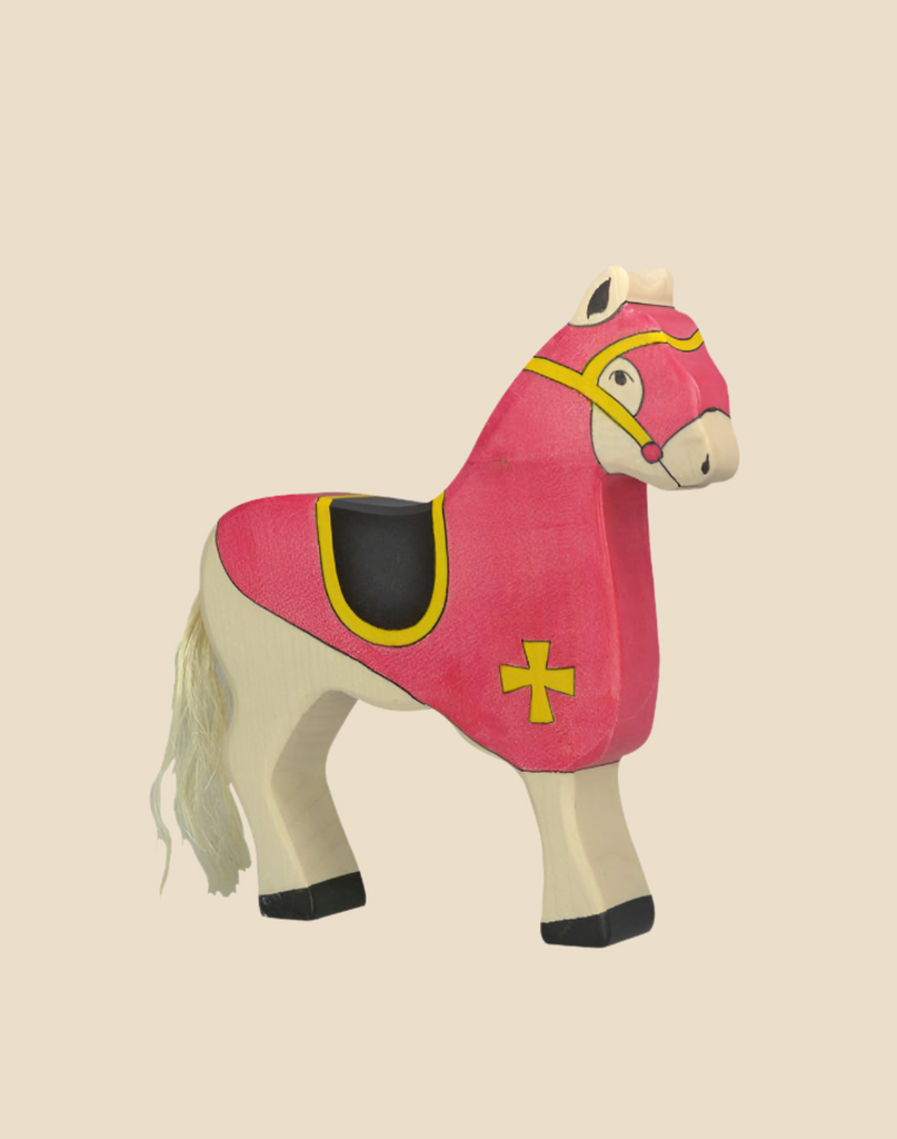 The Holztiger Tournament Horse, Red is a handcrafted wooden toy painted cream with a red and yellow medieval cover, yellow cross, black saddle, and white tail. Ships in one week. Set against a plain beige background.