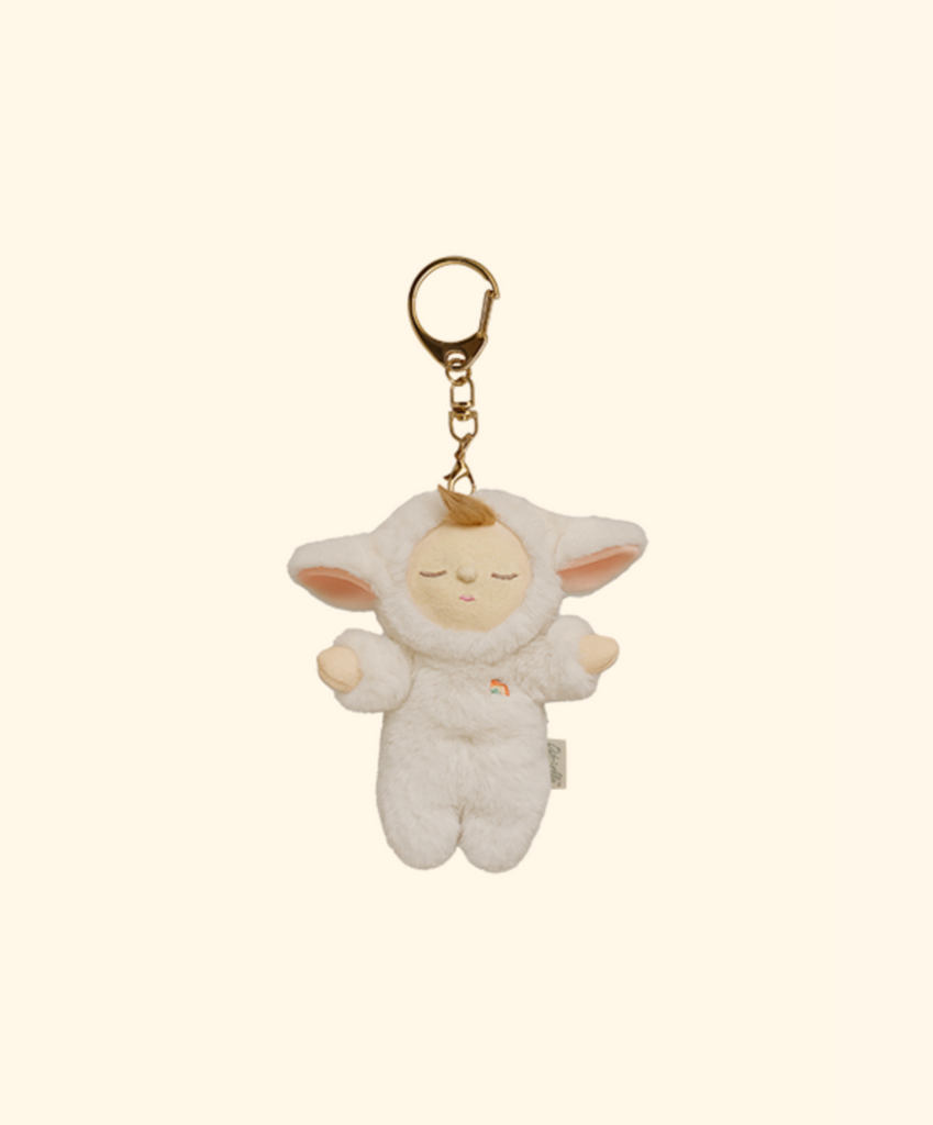 The Olli Ella Cozy Bag Charm - Lamby Pookie is a plush keychain featuring a small doll with closed eyes in a fluffy white lamb costume, big ears, and a gold keyring. Set against a light beige background, it's perfect as a Cozy Dinkum accessory.