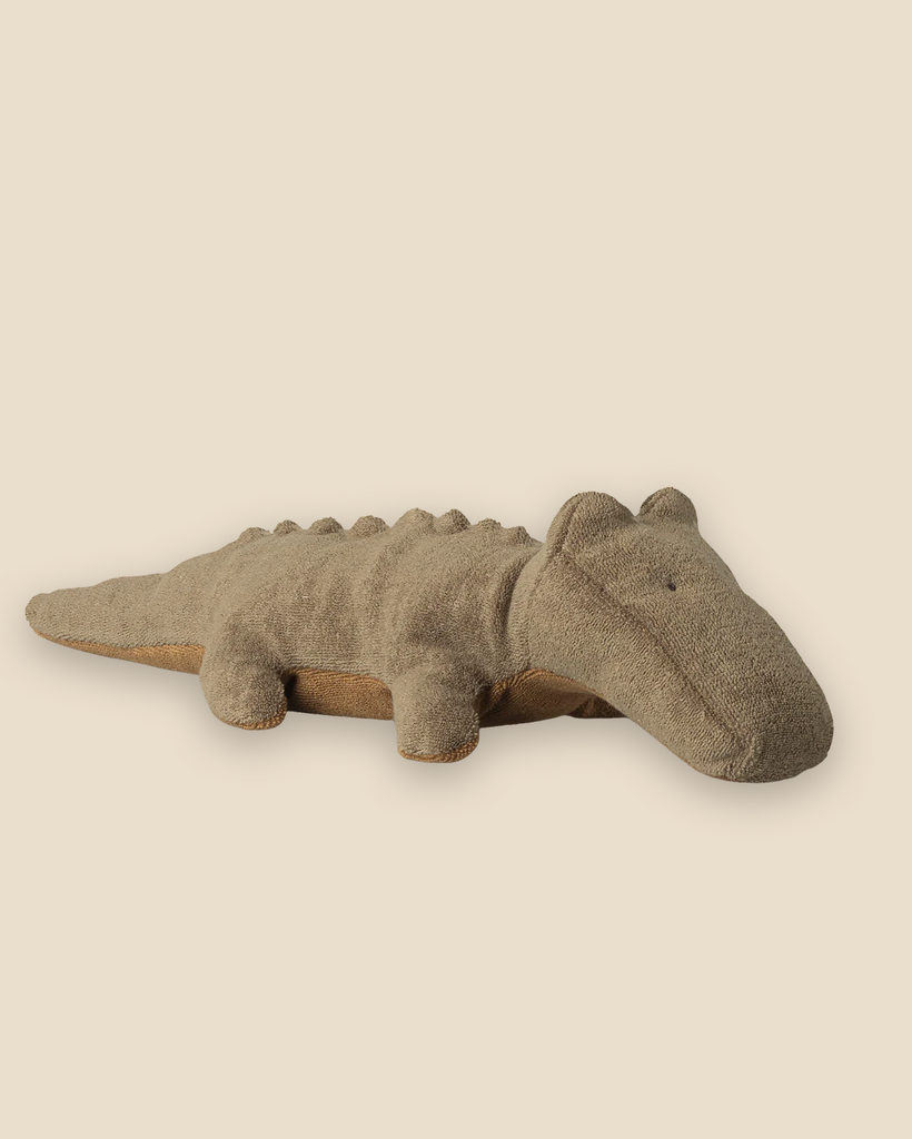 The Pre-order: Maileg Crocodile, Small - Olive Green (expected arrival by 06/15/26) is a soft, plush toy with minimal features and small fabric bumps along its back, shown on a plain light beige background.