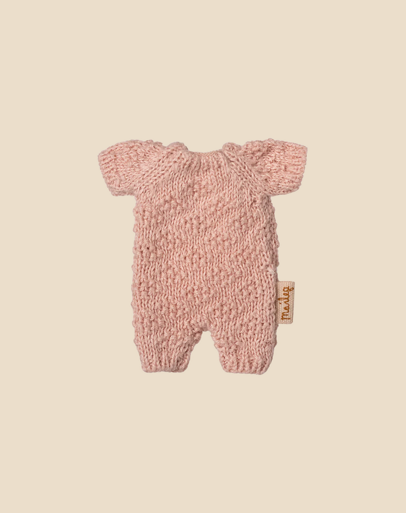 A Maileg Extra Clothing: Knitted Suit, Micro - Rose for Micro Bunny is shown flat on a beige background. The soft pink onesie features short sleeves and legs with a small fabric tag on the right side.
