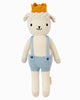 Cuddle + Kind Sebastian the Lamb is a hand-knit doll with a neutral expression, yellow crown, light blue suspenders, and white shorts—crafted with sustainable, fair trade practices.