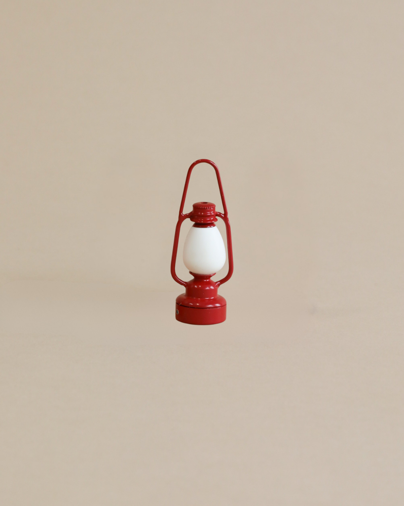 A small, vintage-style red lantern with a white center stands upright against a plain beige background—a charming accessory for any Maileg Little House Bathroom Set.