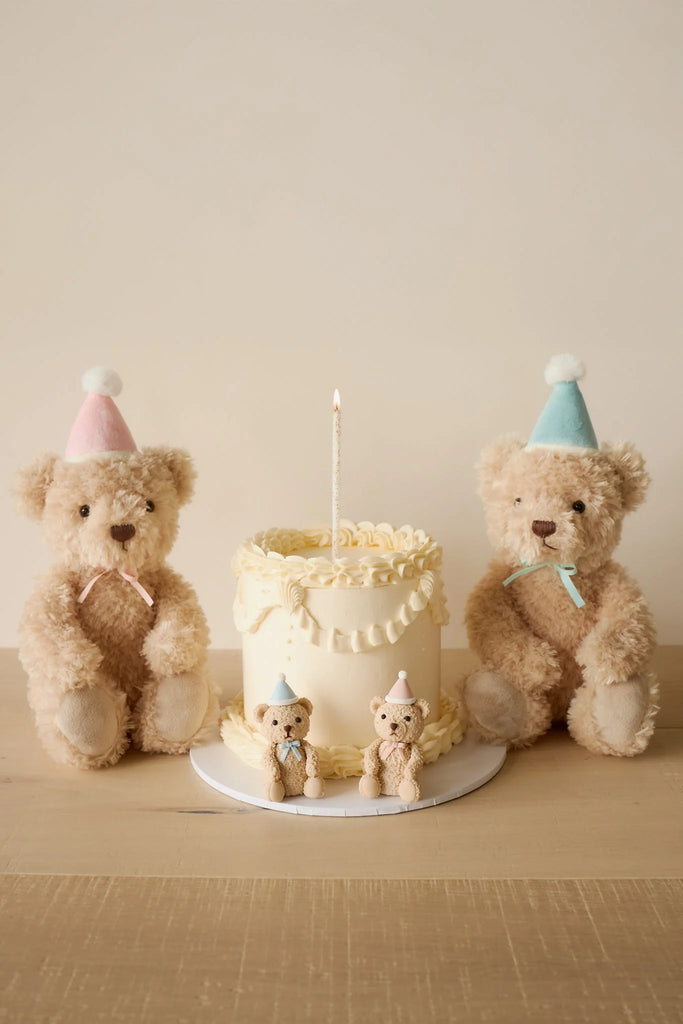 Two Snuggle Bunnies - Birthday Arthur - Sky plush toys in pastel party hats sit beside a white frosted cake with matching bunny toppers, creating a charming keepsake gift scene against a simple beige background.