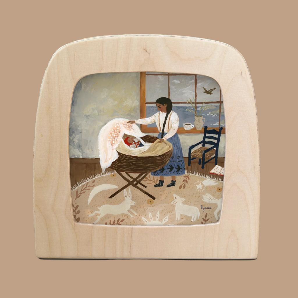 An illustration titled "Silhouette Only - Moment of Tranquility For Toverlux Lamp" depicts a woman in a blue skirt, white blouse tending to a baby in a cradle by a window. A bird casts Magic Silhouettes, with a chair, book, and tea cup accented by an enchanting wooden board. Ships in one week.