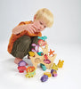 A young child with blond hair plays with a Stacking Coral Reef set, carefully arranging the colorful wooden sea creatures and boat on a white background.