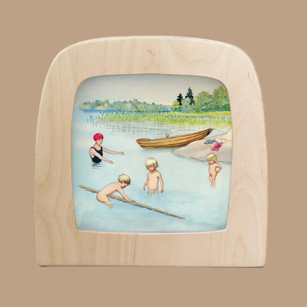 Illustration of three children and an adult enjoying a day at the lake, waist-deep in water with one holding a stick. Bathed in Silhouettes, this scene captures nature and togetherness within its wooden frame. Perfect for the Toverlux Lamp, "Silhouette Only - Around The Year (June).