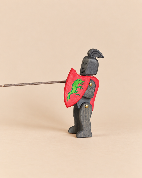 Ostheimer Black Knight handcrafted wooden toy in dark armor, holding a red shield with a green lizard emblem and a long, thin lance for imaginative play.