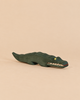 An Ostheimer Crocodile handcrafted wooden figure painted dark green with a yellow eye and visible white teeth, perfect for imaginative play.