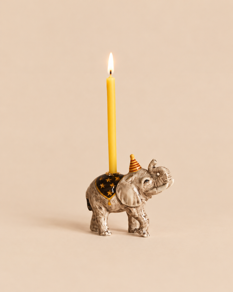 Elephant Cake Topper - Final Sale featuring a ceramic elephant wearing a party hat and a star-patterned blanket, holding a lit yellow taper candle on its back as a handcrafted collectible birthday decoration.