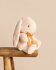 Maileg Plush Bunny, Small - Cream sitting on a wooden stool, featuring long ears and an orange ribbon around its neck.