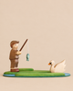A handmade Holzwald Fishing Pond Set features a wooden toy fisherman on a green bank, casting his line toward a white swan floating on a blue pond.