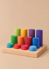 Grimm’s Stacking Game Small Rainbow Rollers featuring ten colorful, cylindrical blocks of varying heights on a wooden base, arranged in a grid for color sorting and motor skills.