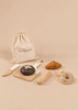 Wooden Bakery Set pieces, including a loaf of bread on a cutting board, a knife, a croissant, a baguette, and two donuts, arranged in front of a drawstring storage bag.