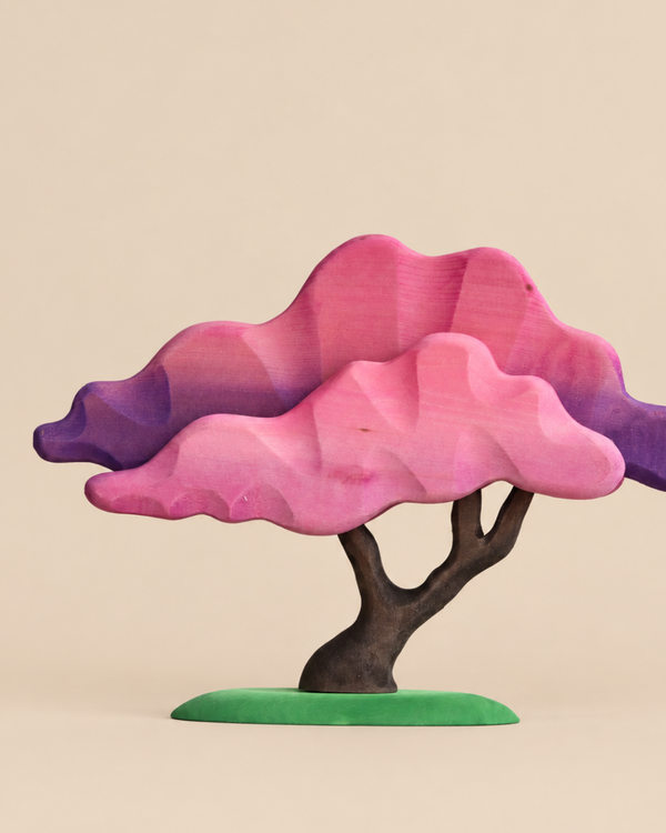 A Bumbu Handmade Wooden Japanese Maple Tree featuring a dark brown trunk, a bright green base, and layered, faceted foliage painted in shades of pink and purple.
