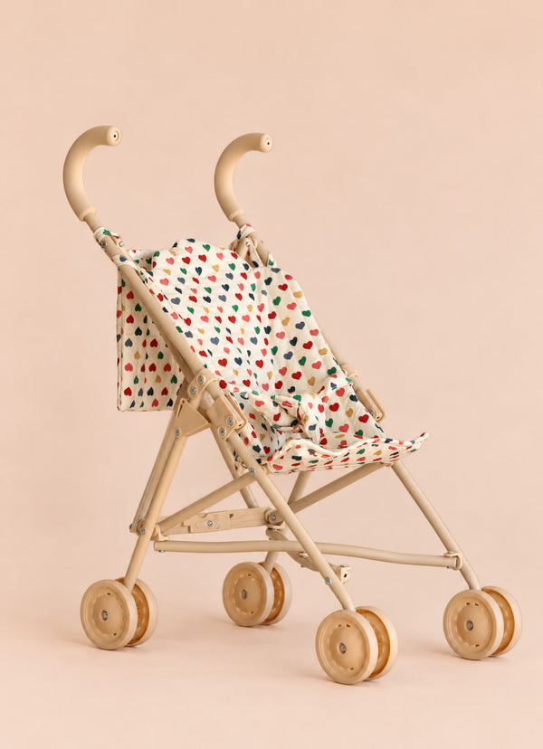 The Konges Sloejd Doll Stroller - Colored Hearts features double wooden wheels and a heart-patterned fabric seat in beige, shown against a plain beige background.