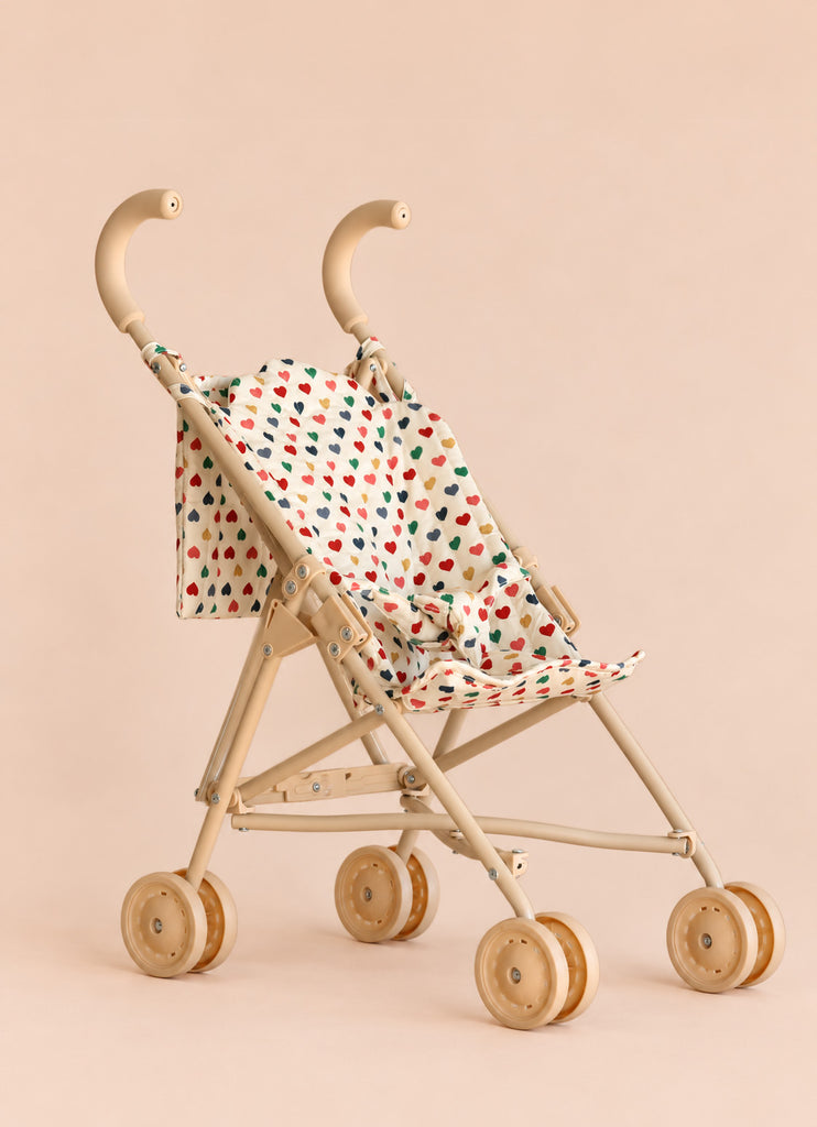The Konges Sloejd Doll Stroller - Colored Hearts features double wooden wheels and a heart-patterned fabric seat in beige, shown against a plain beige background.