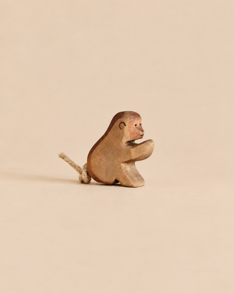 A small, handcrafted wooden Ostheimer Baboon, Sitting with a short rope tail.