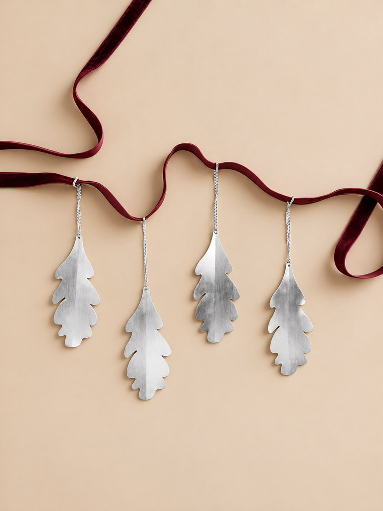 Four Ferm Living Oak Leaf Ornaments - Set of 4 - Silver hanging from a dark red velvet ribbon.