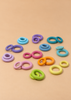 Pairs of pastel Grimm’s Building Rings - Pastel wooden stacking toys arranged on a beige surface.