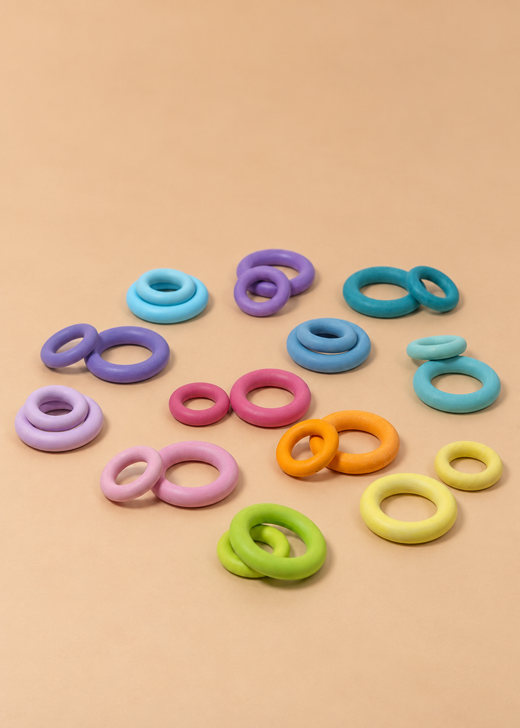Pairs of pastel Grimm’s Building Rings - Pastel wooden stacking toys arranged on a beige surface.