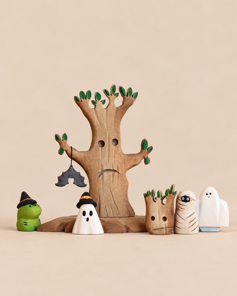 The Handmade Bumbu Haunted Tree Halloween Set features a wooden tree with a hanging bat ornament, surrounded by sustainable Waldorf figures including ghosts, a mummy, and a green creature, all wearing black witch hats.