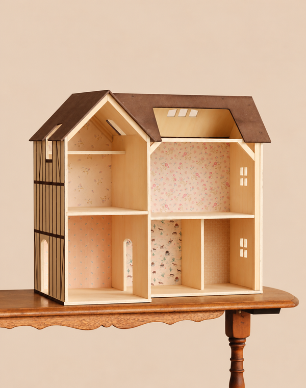 A Maileg Farmhouse Dollhouse with Wallpaper featuring a brown roof and multiple rooms decorated with patterned wallpaper, sitting on a wooden table.