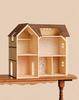 A Maileg Farmhouse Dollhouse with Wallpaper featuring a brown roof and multiple rooms decorated with patterned wallpaper, sitting on a wooden table.