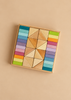A wooden square tray from the Pastel Duo Block Set contains a central cluster of natural wood triangles flanked by columns of pastel building blocks in rainbow gradients.