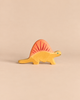 A handcrafted Holztiger Dimetrodon Dinosaur toy with a yellow body and a reddish-orange sail.