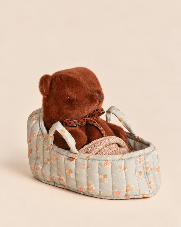 Maileg Teddy Bear in Carry Cot featuring a brown teddy bear with a leopard-print bowtie inside a floral-patterned quilted carry cot.