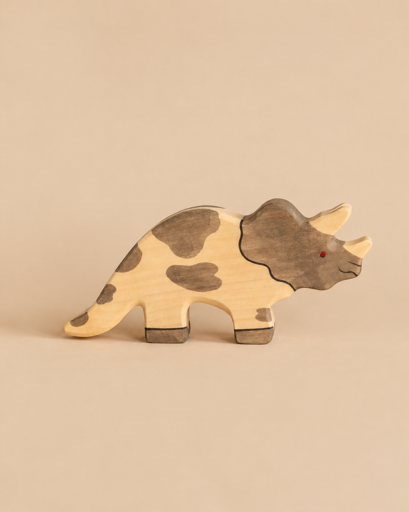 Handcrafted wooden Holztiger Triceratops dinosaur toy with brown spots and a red eye.