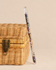 A clear Konges Sloejd Magical Glitter Wand - Star Glitter filled with multicolored star-shaped accents resting against a small wicker box.