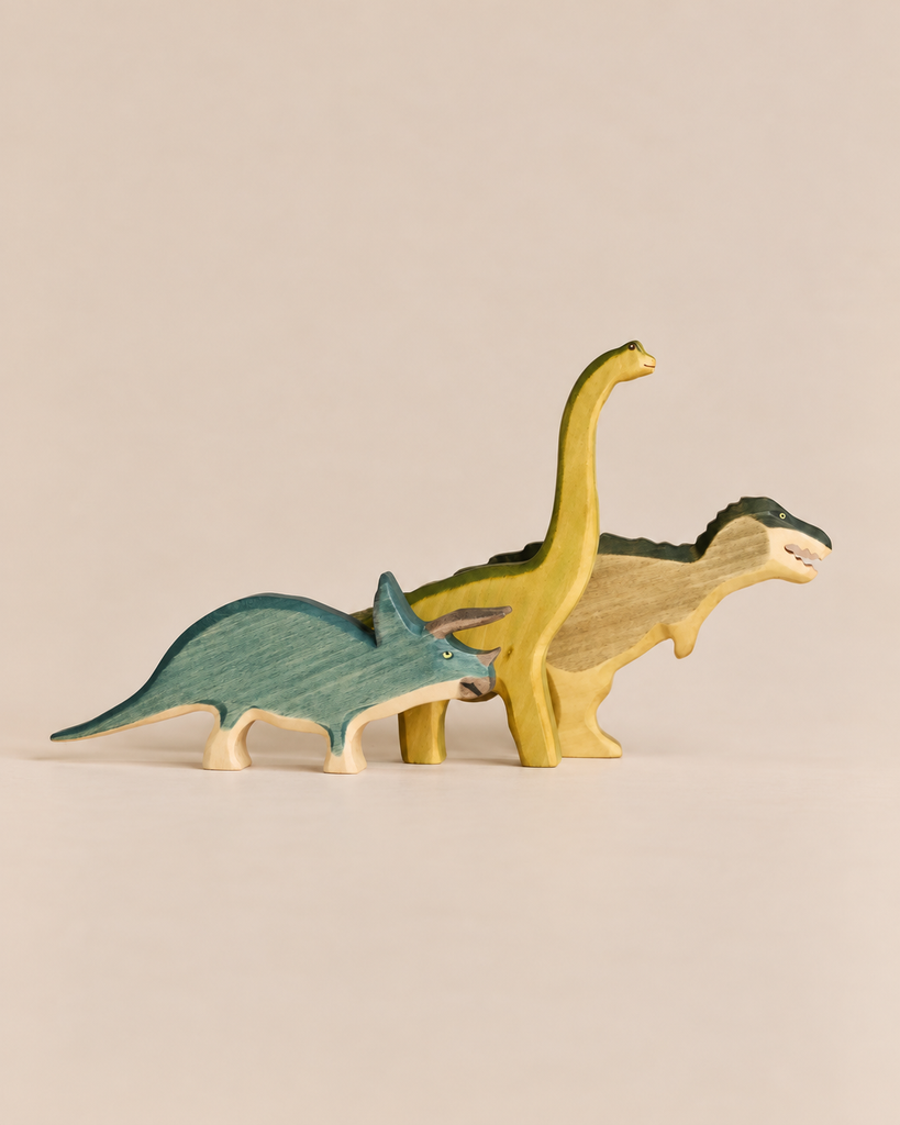 Handmade Holzwald Dinosaur Set featuring three wooden toys: a blue triceratops, a yellow long-necked dinosaur, and a tan and green T-Rex.