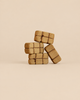 Four handcrafted wooden blocks from the Bumbu Handmade Wooden Haystacks Set, textured to resemble hay bales, stacked together and tied with string for imaginative play.