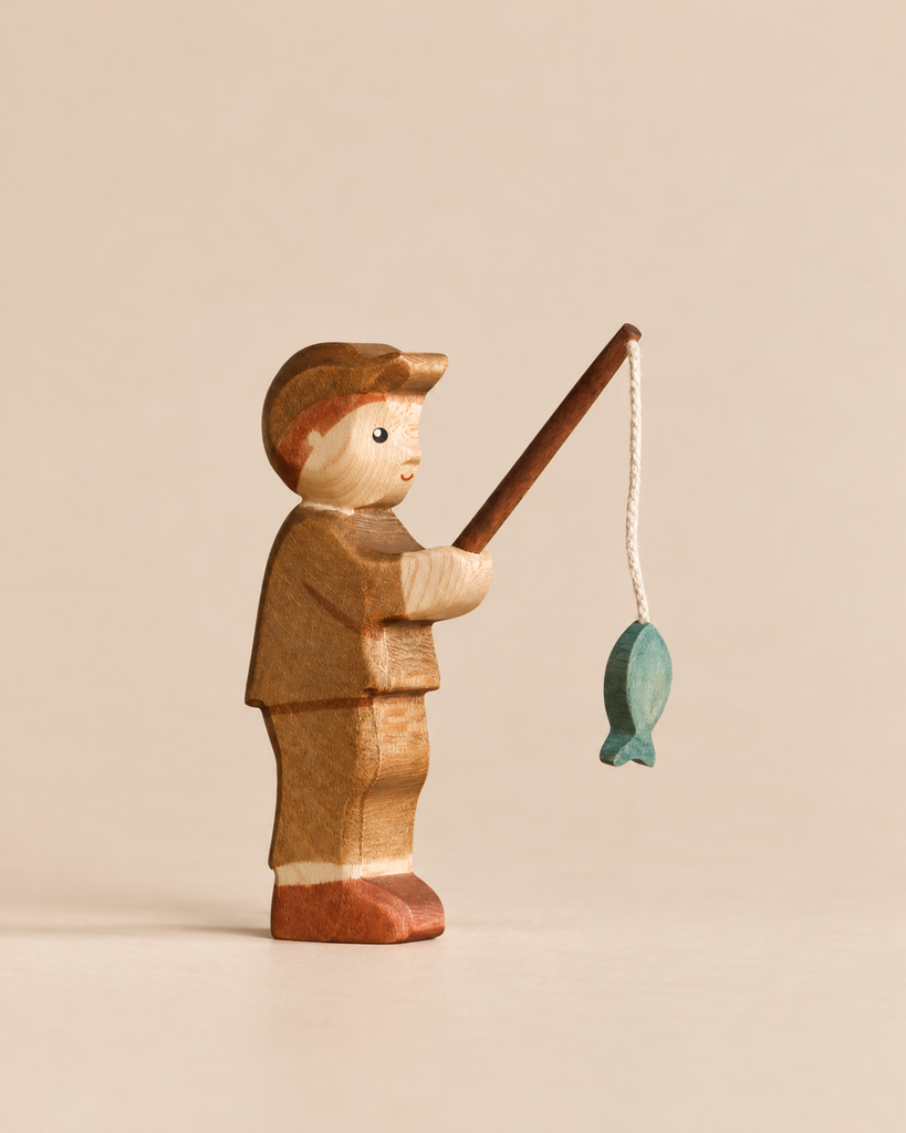 A handmade Holzwald Fishing Pond Set figurine of a person wearing a cap, holding a fishing rod with a small blue fish hanging from the line.