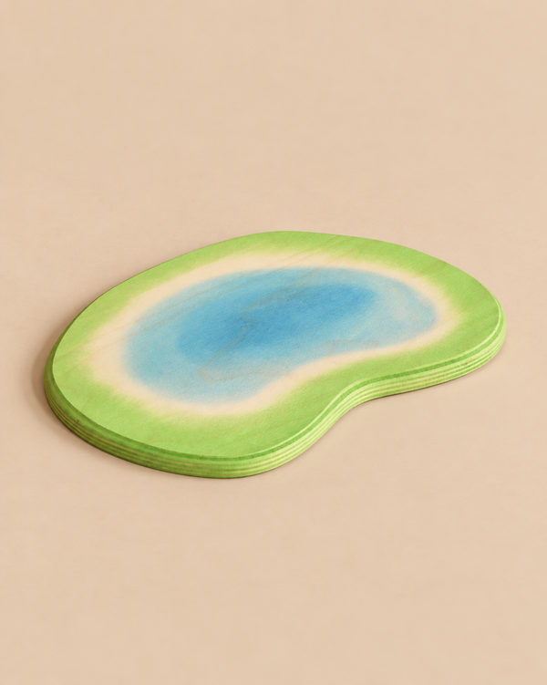 An Ostheimer Pond handcrafted wooden toy piece, flat and kidney-shaped, with a painted blue water center surrounded by a green grassy border.