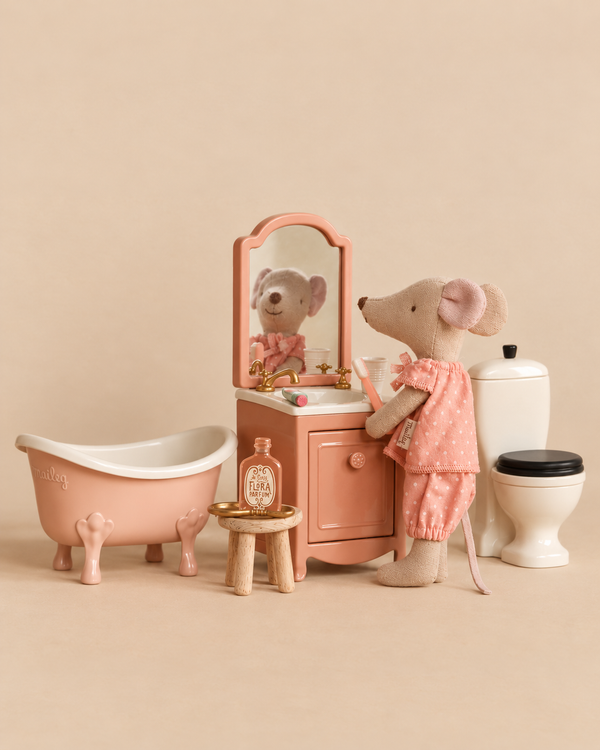 A Maileg Big Sister Bathroom Set features a Big Sister Mouse in pink polka-dot pajamas standing at a miniature vanity with a toothbrush, next to a pink clawfoot bathtub and a toilet.