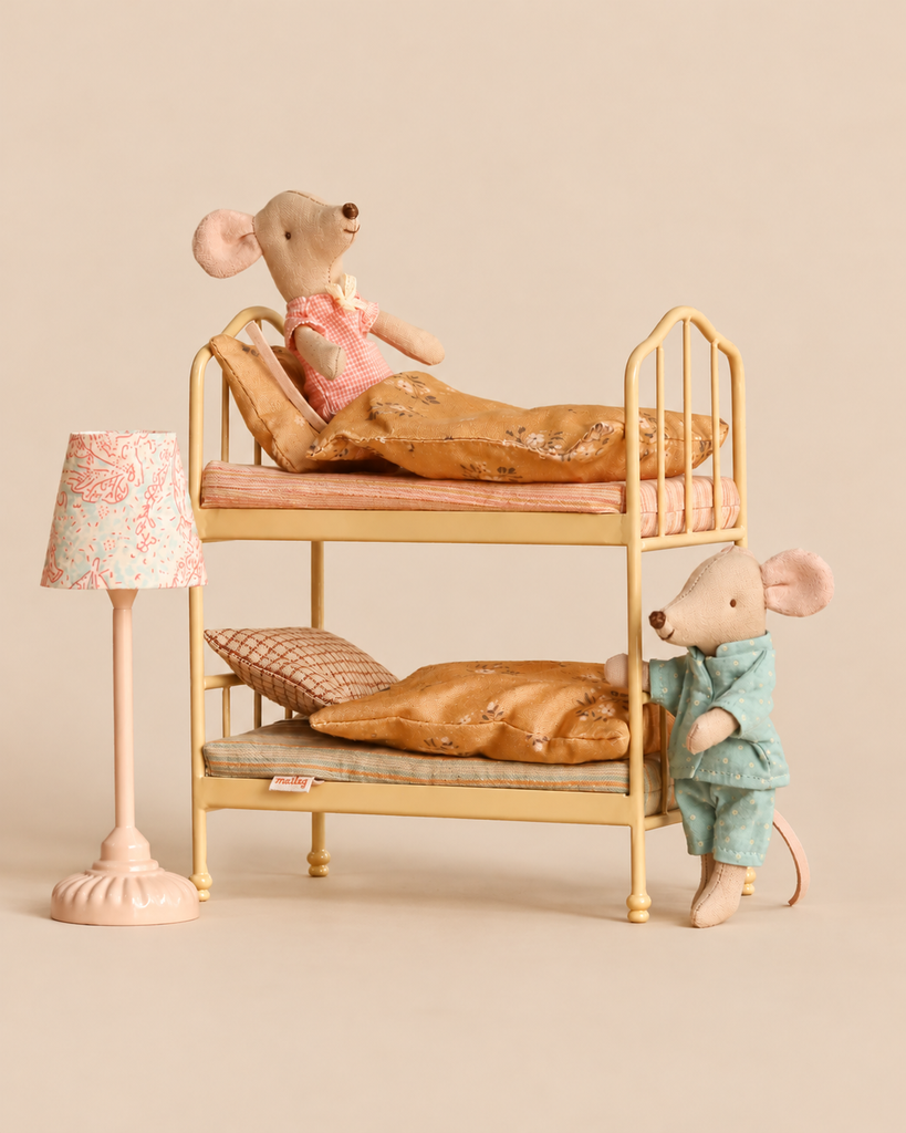 Two Maileg mice in pajamas resting in a Maileg Bunk Bed Bedroom Set with Little Brother & Sister beside a vintage floor lamp.