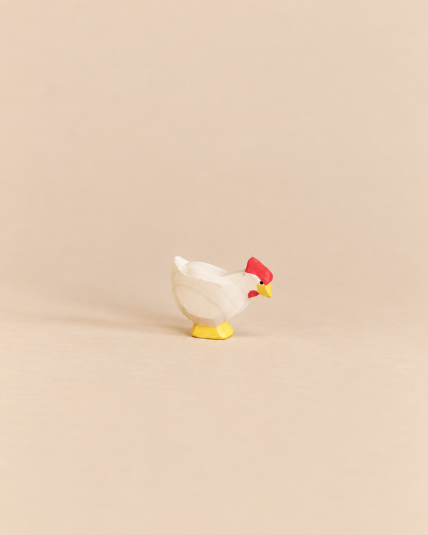 An Ostheimer White Hen - Standing handcrafted as a small wooden toy with a white body, red comb, and yellow feet, perfect for imaginative play.