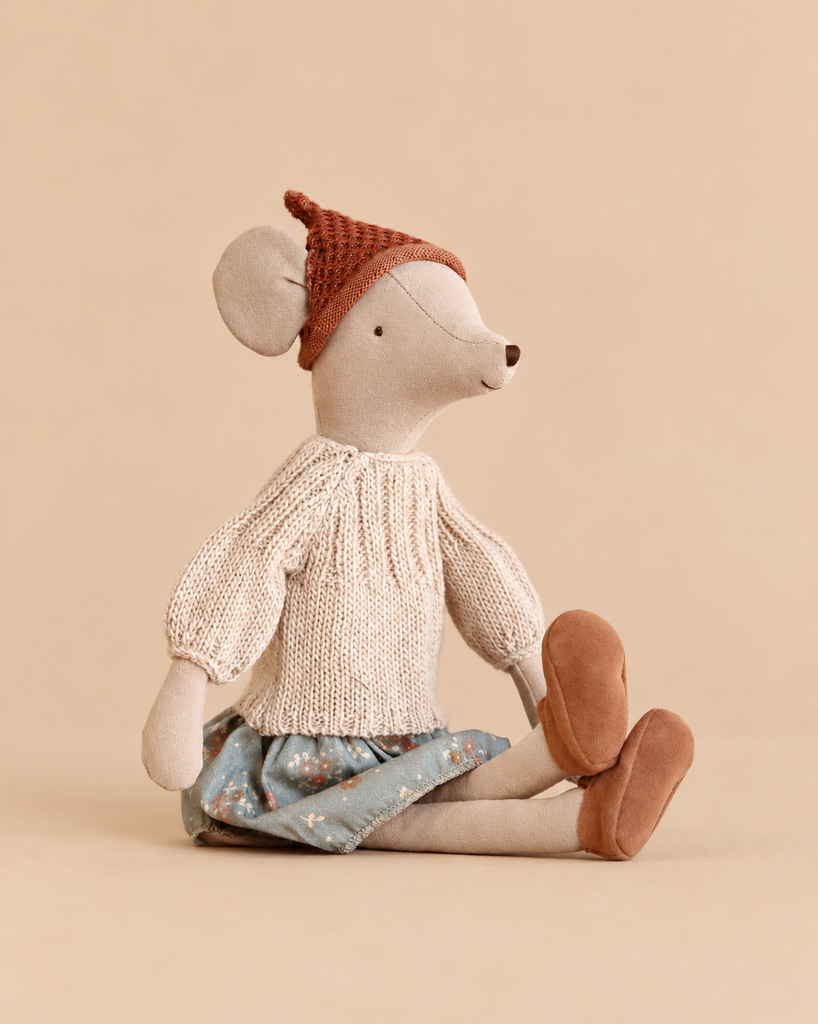 A Maileg Medium Mice Set medium mouse plush doll wearing a brown knitted cap, a ribbed sweater, a floral skirt, and brown shoes, sitting on a solid background.