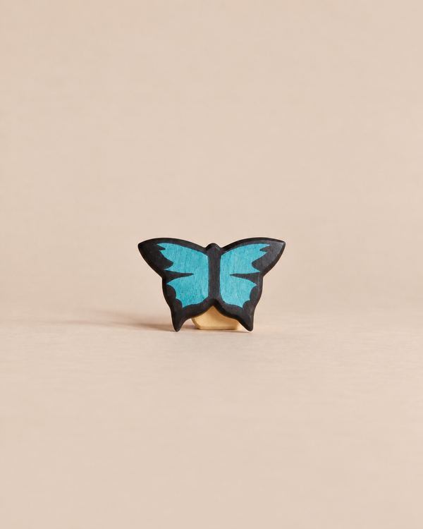 Handmade Holzwald Butterfly, a small, sustainable wooden figurine with black wings featuring bright blue details for imaginative play.