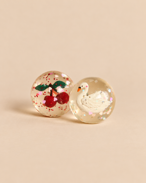Konges Sloejd Glitter Bouncing Ball Set - Cherry & Swan featuring two clear bouncing balls, one with a cherry charm and red glitter, and the other with a white swan figure and heart-shaped confetti.