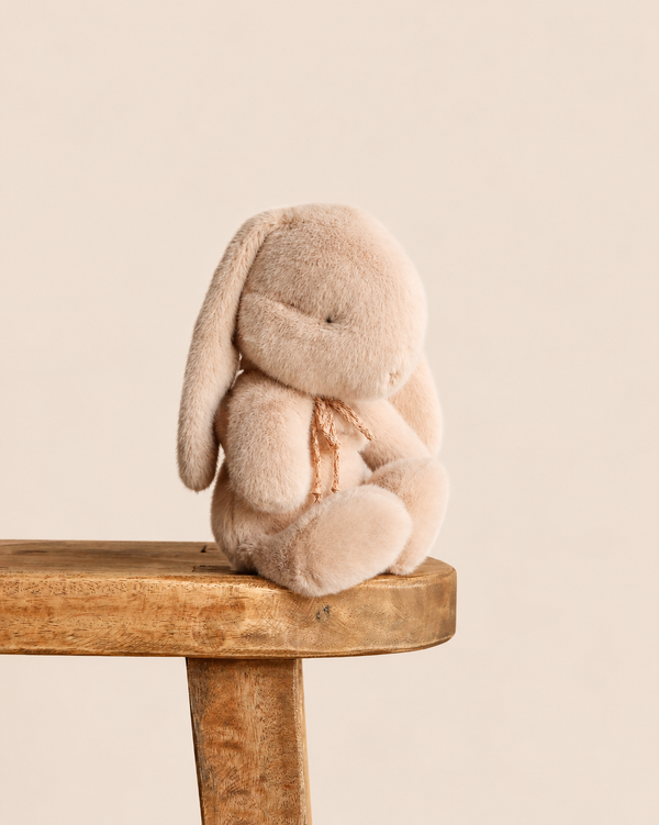 A soft, latte-colored Maileg Plush Bunny, Small with long ears sitting on a wooden stool.