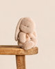 A soft, latte-colored Maileg Plush Bunny, Small with long ears sitting on a wooden stool.
