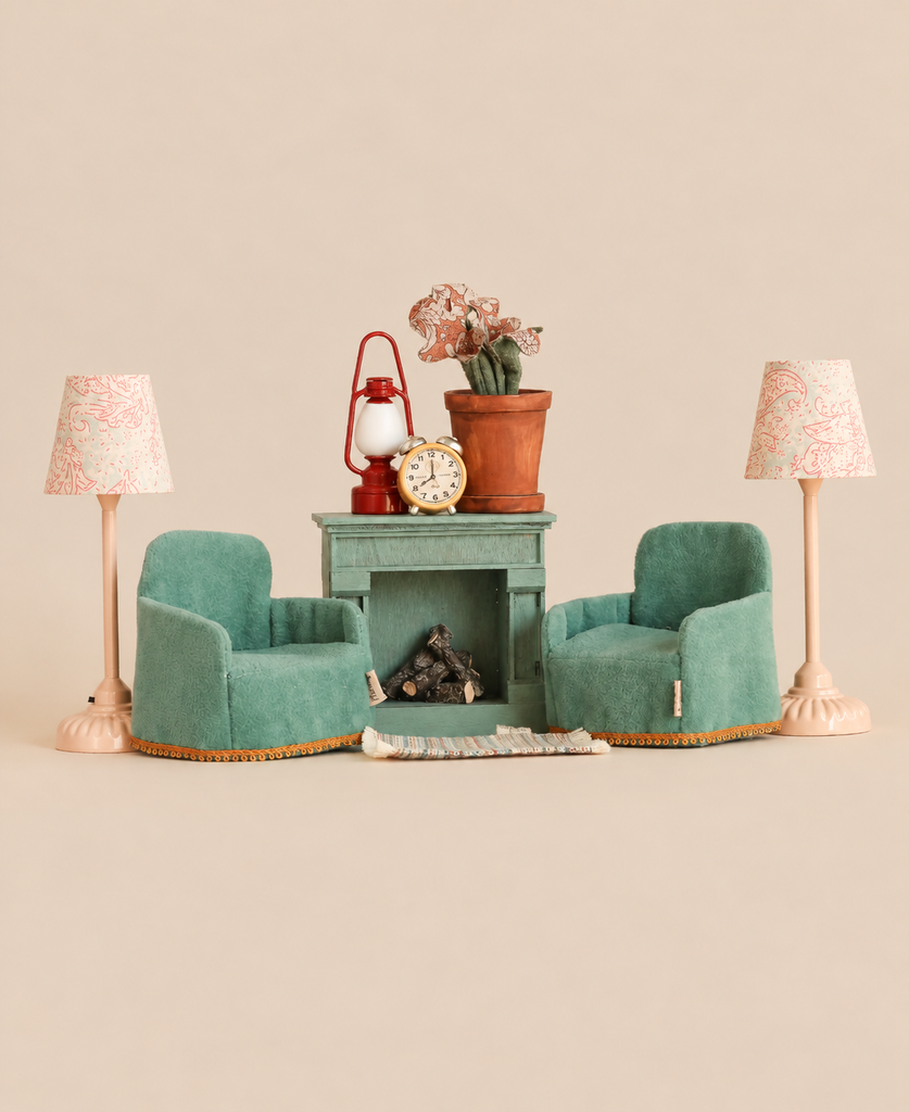 Maileg Family Room Set featuring two teal armchairs, two lamps with patterned shades, and a fireplace mantel holding a lantern, a potted plant, and an alarm clock.