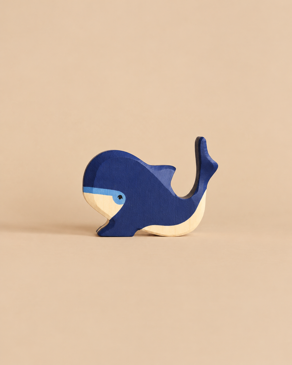 A handcrafted Holztiger Blue Whale toy with a dark blue body, light blue facial details, and a natural wood-colored underside.