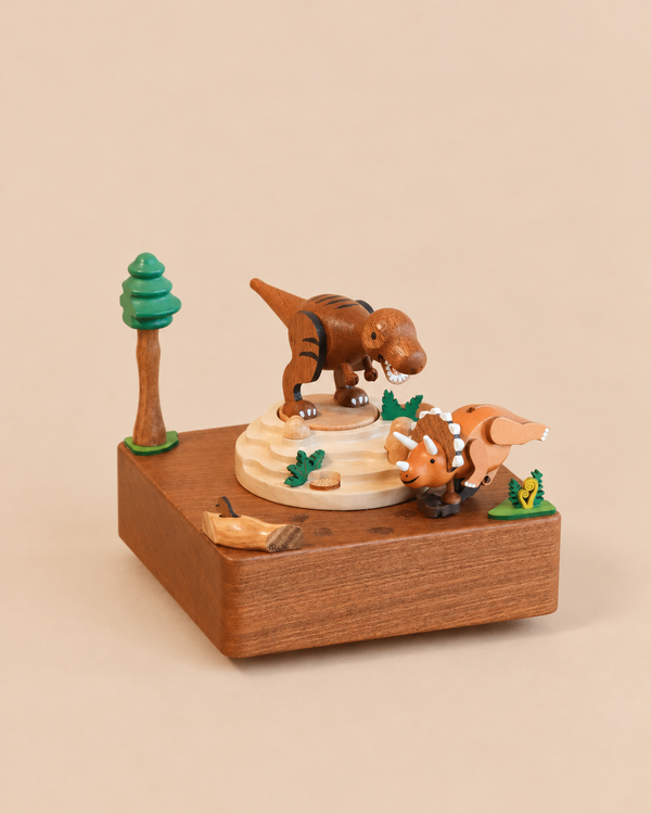 A Wooden Dinosaur Music Box featuring a T-Rex on a raised platform and a triceratops standing below, decorated with a small tree and greenery.